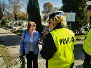 zdjęcie przedstawia policjantów na cmentarzu rozdających elementy odblaskowe.