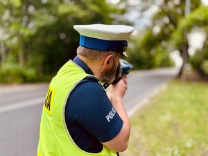 Zdjęcie przedstawia policjanta dokonującego pomiaru prędkości