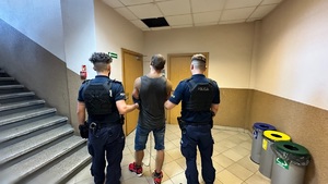 zdjęcie przedstawia zatrzymanego mężczyznę w obecności umundurowanych policjantów