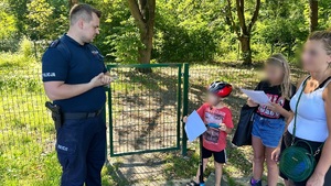 zdjęcie przedstawia policjanta rozdającego ulotki dzieciom na skateparku