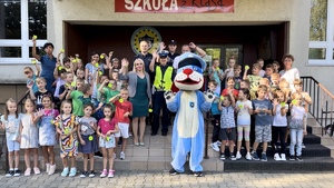 Zdjęcie przedstawia policjantów i Sznupka w trakcie prelekcji dla dzieci pozujących do grupowego zdjęcia na schodach szkoły