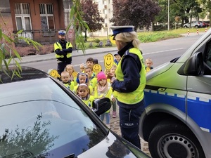 zdjęcie przedstawia dzieci wręczające kierowcy medalion uśmiechu w towarzystwie policjantki