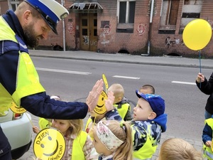 zdjęcie przedstawia dziecko stojące w grupie przybijające &quot;piątkę&quot; policjantowi