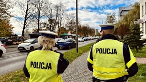 zdjęcie przedstawia policjantów w kamizelkach odblaskowych idących chodnikiem