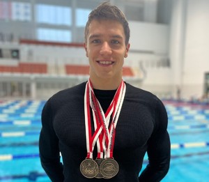 Na zdjęciu widoczny mężczyzna z medalami na szyi, w tle widać basen