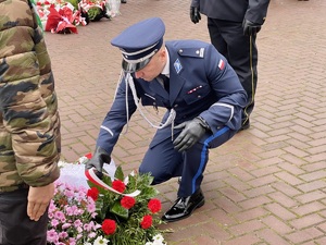 zdjęcie przedstawia policjanta w mundurze galowym skłądającego wieniec pod pomnikiem