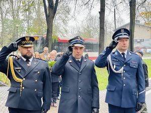 zdjęcie przedstawia przedstawicieli Straży Miejskiej, Policji i Straży Pożarnej w mundurach galowych stojących przed pomnikiem i oddających honory