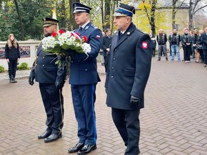 zdjęcie przedstawia przedstawicieli Straży Miejskiej, Policji i Straży Pożarnej w mundurach galowych stojących przed pomnikiem