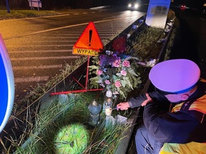 zdjęcie przedstawia policjanta zapalającego świeczkę przy krzyżu