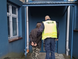 zdjęcie przedstawia policjanta prowadzącego zatrzymanego