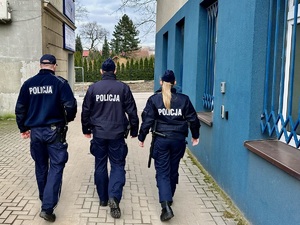 Zdjęcie przedstawia trójkę policjantów przechodzących przez podwórko