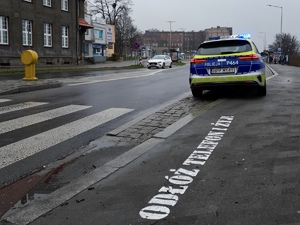 zdjęcie przedstawia radiowóz stojący przy przejściu dla pieszych, przed przejściem na chodniku napis Odłóż telefon i żyj.