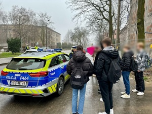 zdjęcie przedstawia młodzież z którą rozmawia policjantka, w tle radiowóz