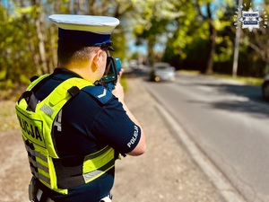 zdjęcie przedstawia policjanta w trakcie pomiaru prędkości pojazdów