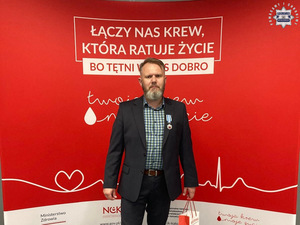 zdjęcie przedstawia meżczyznę w garniturze pozującego z medalem