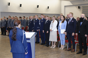 zdjęcie przedstawia policjantkę odczytującą rozkazy personalne, w tle policjanci i goście honorowi stojący.