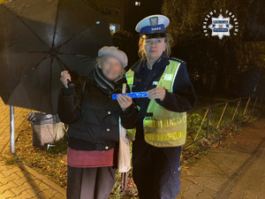 zdjęcie przedstawia policjantkę rozdającą elementy odblaskowe