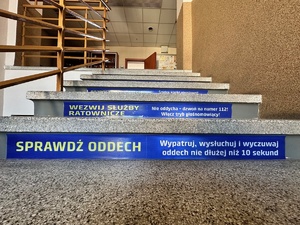 zdjęcie przedstawia naklejkę na schodach z napisem Sprawdź oddech Wypatruj, wysłuchuj i wyczuwaj oddech nie dłużej niż 10 sekund