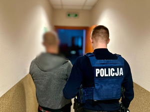 zdjęcie przedstawia zatrzymanego prowadzonego przez policjanta