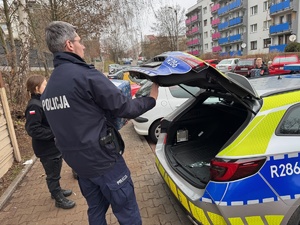 zdjęcie przedstawia policjanta doręczającego paczkę do potrzebujących rodzin