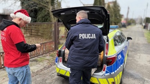 zdjęcie przedstawia policjanta doręczającego paczkę do potrzebujących rodzin