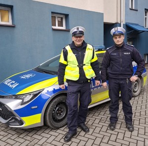 Na zdjęciu dwóch policjantów w umundurowaniu oraz radiowóz Policji.