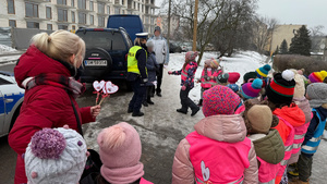 zdjęcie przedstawia dziecko wraz z policjantką wręczające serduszko seniorowi