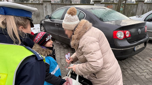 zdjęcie przedstawia dziecko wraz z policjantką wręczające serduszko seniorowi