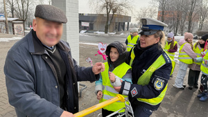 zdjęcie przedstawia dziecko wraz z policjantką wręczające serduszko seniorowi