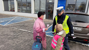 zdjęcie przedstawia dziecko wraz z policjantką wręczające serduszko seniorowi