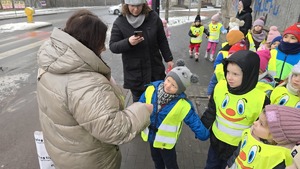 zdjęcie przedstawia policjantkę i dzieci w trakcie rozdawania serduszek uczestnikom ruchu drogowego