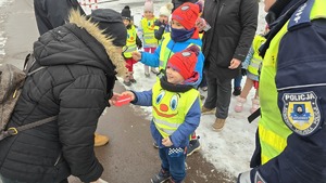 zdjęcie przedstawia policjantkę i dzieci w trakcie rozdawania serduszek uczestnikom ruchu drogowego