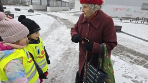 zdjęcie przedstawia policjantkę i dzieci w trakcie rozdawania serduszek uczestnikom ruchu drogowego