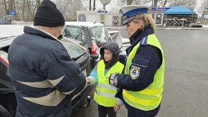 zdjęcie przedstawia policjantkę i dzieci w trakcie rozdawania serduszek uczestnikom ruchu drogowego