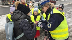 zdjęcie przedstawia policjantkę i dzieci w trakcie rozdawania serduszek uczestnikom ruchu drogowego