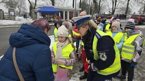 zdjęcie przedstawia policjantkę i dzieci w trakcie rozdawania serduszek uczestnikom ruchu drogowego