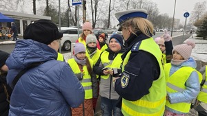 zdjęcie przedstawia policjantkę i dzieci w trakcie rozdawania serduszek uczestnikom ruchu drogowego