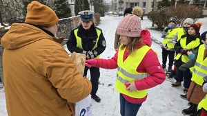 zdjęcie przedstawia policjantkę i dzieci w trakcie rozdawania serduszek uczestnikom ruchu drogowego