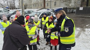 zdjęcie przedstawia policjantkę i dzieci w trakcie rozdawania serduszek uczestnikom ruchu drogowego