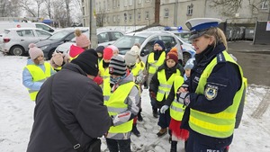 zdjęcie przedstawia policjantkę i dzieci w trakcie rozdawania serduszek uczestnikom ruchu drogowego