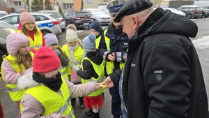 zdjęcie przedstawia policjantkę i dzieci w trakcie rozdawania serduszek uczestnikom ruchu drogowego