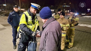 zdjęcie przedstawia policjantów, strażaków i strażników miejskich rozdających odblaski przechodniom