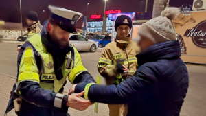 zdjęcie przedstawia policjantów, strażaków i strażników miejskich rozdających odblaski przechodniom