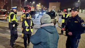 zdjęcie przedstawia policjantów, strażaków i strażników miejskich rozdających odblaski przechodniom