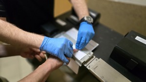 zdjęcie przedstawia ręce policjanta, który pobiera odciski palców od zatrzymanego