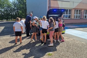 zdjęcie przedstawia dzielnicowego pokazujący dzieciom radiowóz.