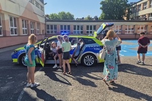 zdjęcie przedstawia dzielnicowego pokazujący dzieciom radiowóz.