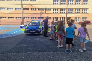 zdjęcie przedstawia dzielnicowego pokazujący dzieciom radiowóz.