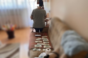 zdjęcie przedstawia starszą osobę rozmawiającą przez telefon. Widoczne pieniądze przygotowane dla sprawcy oszustwa