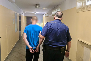 zdjęcie przedstawia zatrzymanego prowadzonego w kajdankach przez policjanta